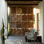 Krytá drevená terasa so stenou na palivové drevo, prútenými kreslami a podhľadom z tmavých masívnych dosiek.