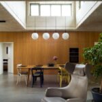 Moderný interiér s dreveným obkladom steny, sivou betónovou podlahou, jedálenským stolom a dizajnovým koženým kreslom.