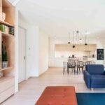 Svetlý, otvorený interiér s drevenou podlahou, policovým regálom z brezovej preglejky a modernou jedálenskou a kuchynskou časťou v béžových tónochSvetlý, otvorený interiér s drevenou podlahou, policovým regálom z brezovej preglejky a modernou jedálenskou a kuchynskou časťou v béžových tónoch.