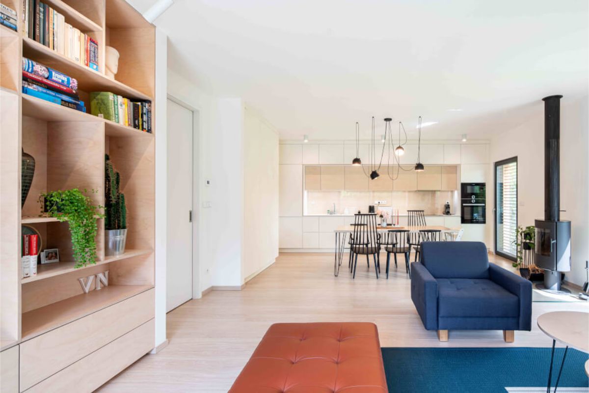 Svetlý, otvorený interiér s drevenou podlahou, policovým regálom z brezovej preglejky a modernou jedálenskou a kuchynskou časťou v béžových tónochSvetlý, otvorený interiér s drevenou podlahou, policovým regálom z brezovej preglejky a modernou jedálenskou a kuchynskou časťou v béžových tónoch.