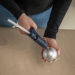 Detail lepenia tavnou pištoľou na vianočnú guľu.