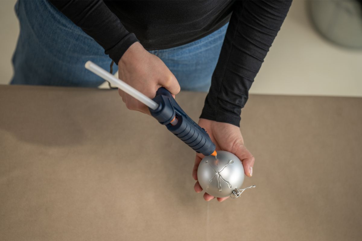 Detail lepenia tavnou pištoľou na vianočnú guľu.