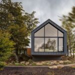 Moderný chalet so sivou fasádou a preskleným štítom v prírodnom prostredí.