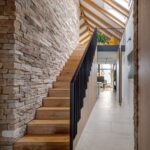 Drevené schodisko s čiernym zábradlím vedľa masívneho kamenného obkladu steny.