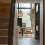 Pohľad z chodby na jedálenskú časť s prúteným lustrom, dreveným stolom a kamenným pilierom.