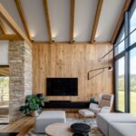 Moderná obývacia izba s dreveným a kamenným obkladom na stenách svetlým sedením a preskleným štítom.