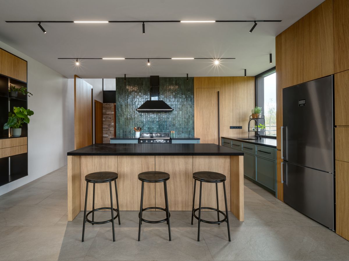 Kuchyňa s drevenými obkladmi, modernou linkou s ostrovčekom s barovým sedením a výrazným tmavozeleným obkladom.