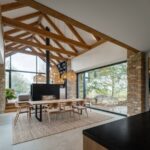 Jedálenský stôl so stoličkami pri kozube uprostred miestnosti a veľkoformátových oknách.