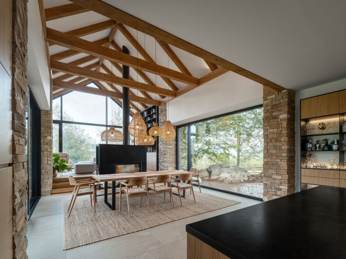 Jedálenský stôl so stoličkami pri kozube uprostred miestnosti a veľkoformátových oknách.