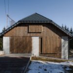Fasáda stodoly s vertikálnym dreveným obkladom a štyrmi zatvorenými drevenými dverami.