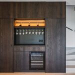 Vstavaný barový kút z tmavého moreného dubu s integrovanou vinotékou, držiakmi na poháre a jemným LED podsvietením.