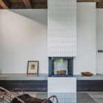 Minimalistický krb obložený bielym štruktúrovaným obkladom s betónovou lavicou a tmavými zásuvkami.