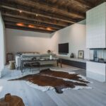 Svetlá obývacia izba s krbom, sivou sedačkou, hovädzou kožou na podlahe a veľkým presklením v škandinávskom štýle.