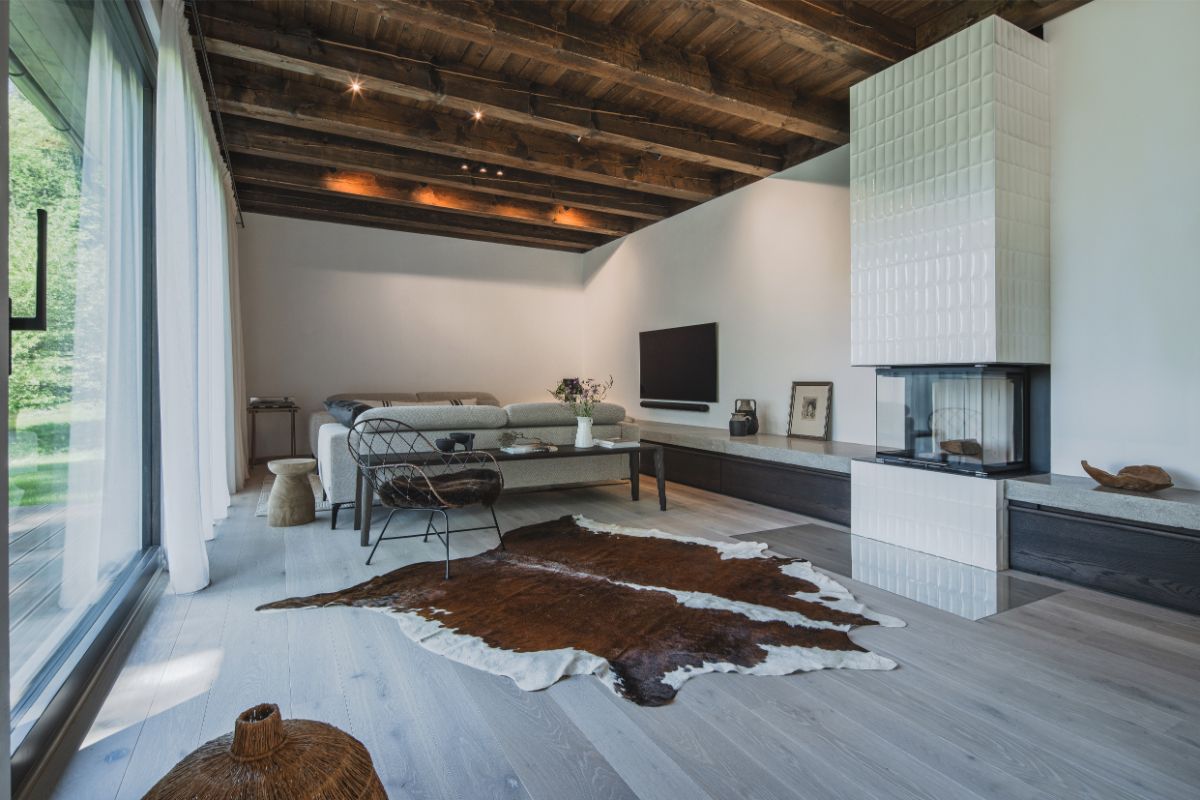 Svetlá obývacia izba s krbom, sivou sedačkou, hovädzou kožou na podlahe a veľkým presklením v škandinávskom štýle.