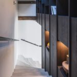 Schodisko zo svetlého dreva s tmavou policovou stenou z dubovej dyhy, integrovaným osvetlením a dekoratívnou keramikou.