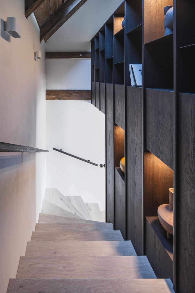 Elegantné schodisko s drevenými stupňami sprevádza po pravej strane vstavaný nábytok. Ponúka štýlové úložné riešenie a priestor na dekorácie.