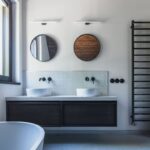 Kúpeľňa s dvojumývadlom na tmavom podvesnom stolíku, bielym vertikálnym obkladom, kruhovými zrkadlami a čiernymi batériami.