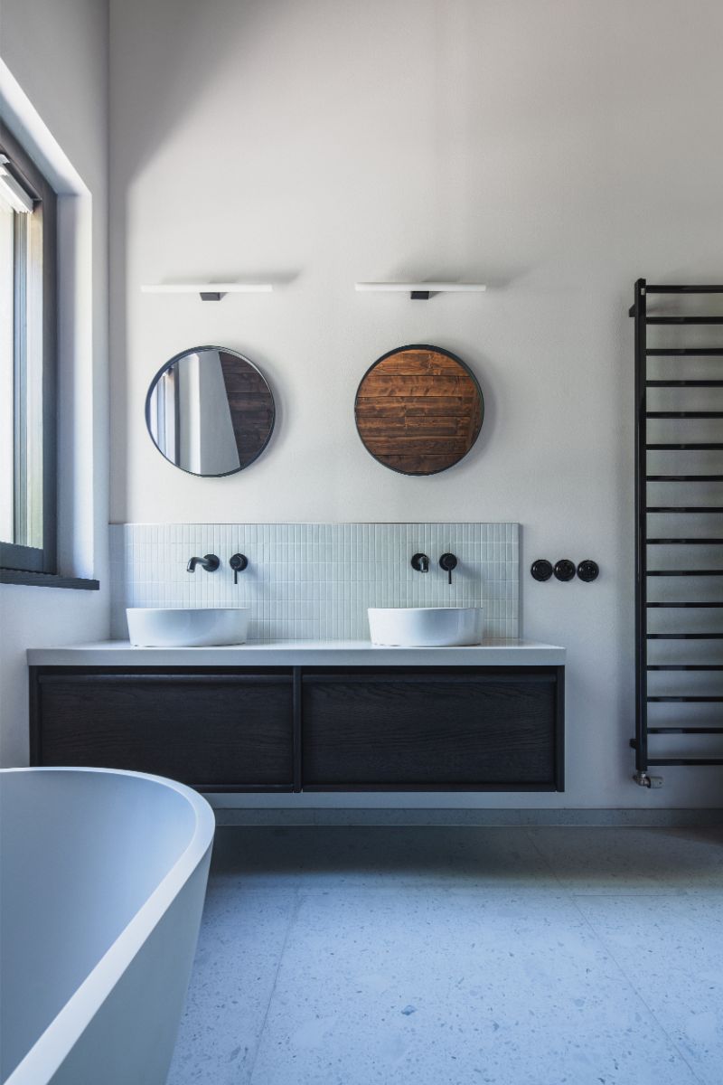 Kúpeľňa s dvojumývadlom na tmavom podvesnom stolíku, bielym vertikálnym obkladom, kruhovými zrkadlami a čiernymi batériami.