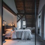 Podkrovná spálňa s masívnym trámovým stropom, posteľou v neutrálnych tónoch, dizajnovými lampami a čiastočne presklenou stenou do kúpeľne