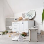 Interiér s polámaným nábytkom, odpasnutým zrkadlom a neporiadkom na zemi.