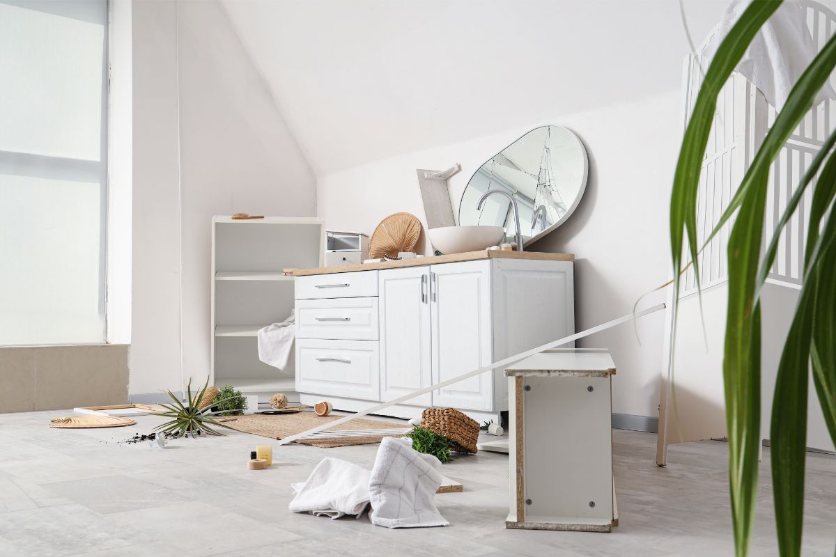 Interiér s polámaným nábytkom, odpasnutým zrkadlom a neporiadkom na zemi.