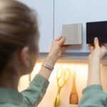 Mladá žena porovnáva dve vzorky materiálov k dvierkam kuchynskej linky.