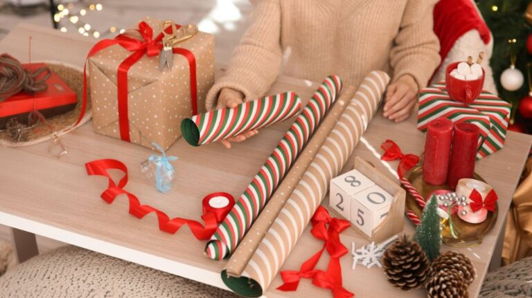 Mladá žena pri balení vianočných darčekov s baliacom papierom na stole.