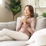 Žena na gauči s hrnčekom v ruke si užíva príjemnú vôňu.