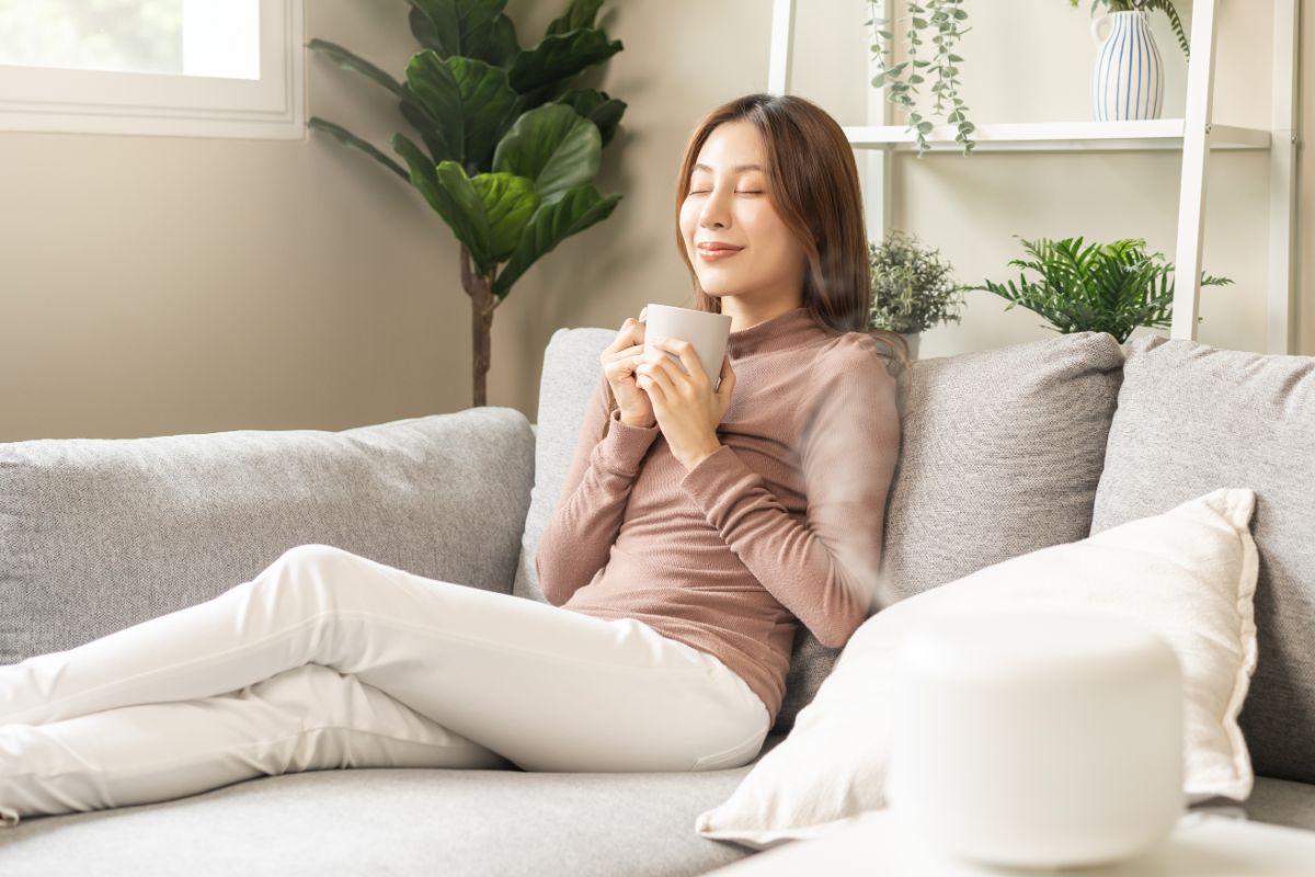 Žena na gauči s hrnčekom v ruke si užíva príjemnú vôňu.