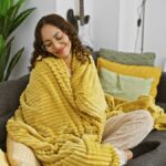 Mladá žena zabalená v deke na sedačke.