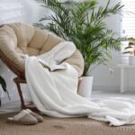 Okrúhle mäkké kreslo s dekou a knihou a papučami vedľa neho.