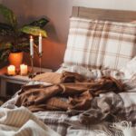 Detail na posteľ s flanelovými obliečkam, dekou a sviečkami na nočnom stolíku.