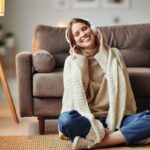 Mladá žena zabalená v deke pri počúvaní hudby cez slúchadlá.