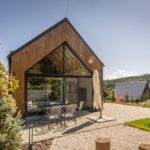 Moderná drevená chata so šikmou strechou a veľkým preskleným štítom, s terasou s posedením a štrkovou záhradou.