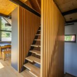 Interiérové drevené schodisko s čiernou kovovou konštrukciou a vertikálnymi drevenými lamelami, s drevenou podlahou a stropom.