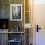 Stena s drevenými lamelami, betónovou omietkou, obrazom lesa a policou s kanvicou.