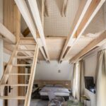 Podkrovný apartmán s drevenými trámami a rebríkom vedúcim na medziposchodie so sieťou.