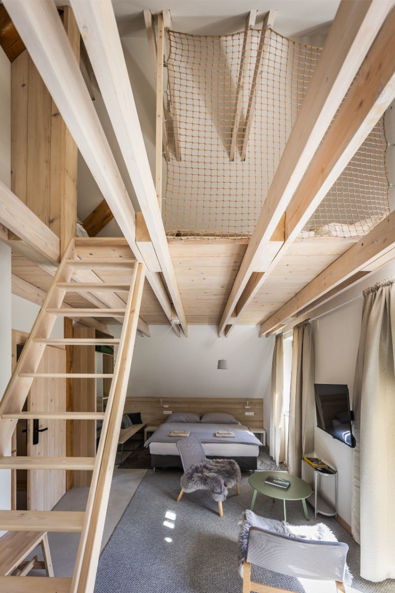 Podkrovný apartmán s drevenými trámami a rebríkom vedúcim na medziposchodie so sieťou.