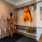 Chodba s dreveným obkladom, lyžiarskym vybavením a oranžovou bundou na vešiakoch.