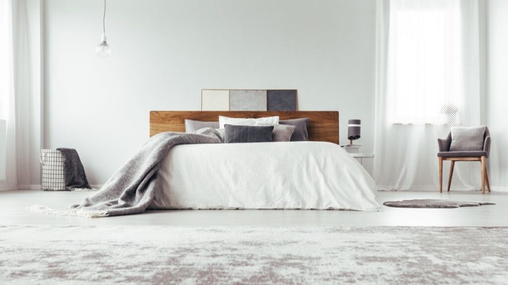 Drevená posteľ s bielou prikrývkou v bielej miestnosti.