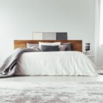 Drevená posteľ s bielou prikrývkou v bielej miestnosti.