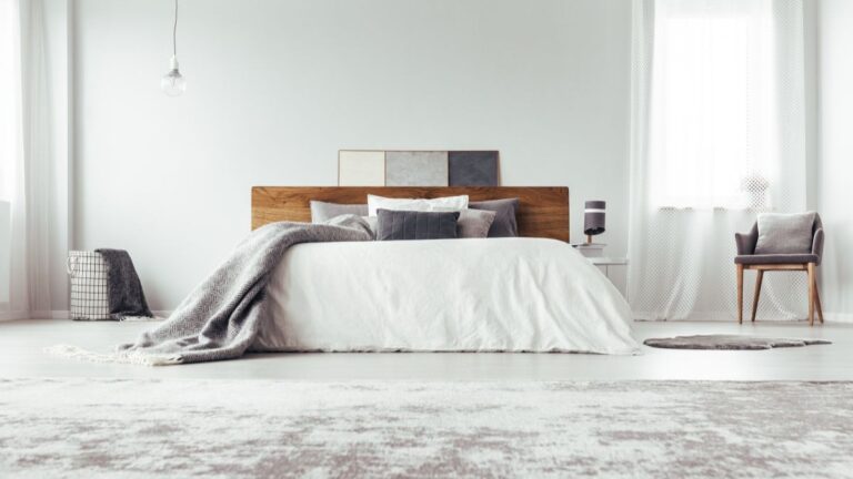 Drevená posteľ s bielou prikrývkou v bielej miestnosti.