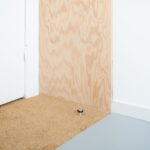 Detail podlahy s prechodom z modrého linolea na drevný panel pri dvernom doraze.