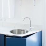 uchyňa s tmavomodrými skrinkami, bielym mramorovým povrchom a antikorovým drezom s oblou chrómovou batériou.