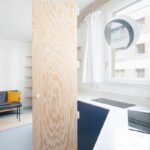 Kuchynský kút s bielym mramorovým obkladom, modrými skrinkami a veľkými drevenými dverami oddeľujúcimi priestor.