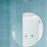 Detail okrúhleho zrkadla na stene obloženej tyrkysovým obkladom.