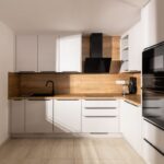 Biela rohová kuchynská linka v tvare L s drevenou pracovnou doskou a čiernou digestorovou stenou v modernom štýle.