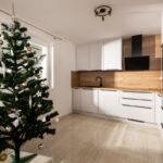 Svetlá moderná kuchyňa s bielymi skrinkami, dubovým dekorom na zástene a tmavými úchytkami vedľa vianočného stromčeka.