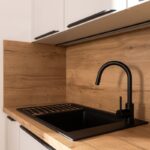 Čierny kuchynský drez s vysokou batériou osadený v pracovnej doske s dekorom prírodného duba.