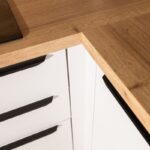 Spoj dvoch častí drevenej pracovnej dosky v rohu bielej kuchynskej linky s lineárnymi čiernymi úchytkami.